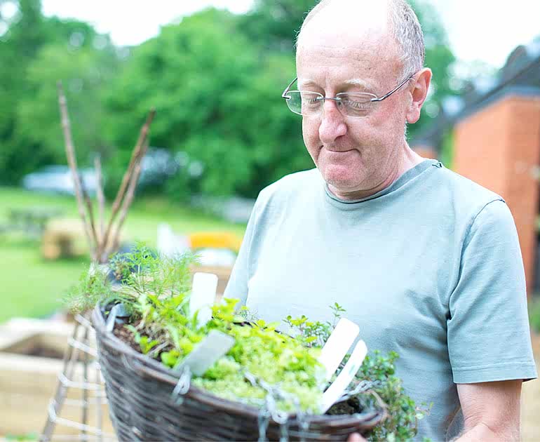 A volunteer in a green shirt holding a hanging basket in the MERL garden.