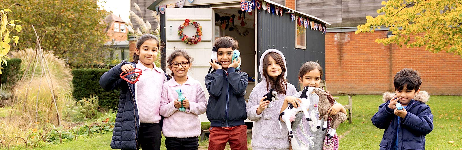 Children in the MERL garden holding up knitted toys from the Shepherd's Hut